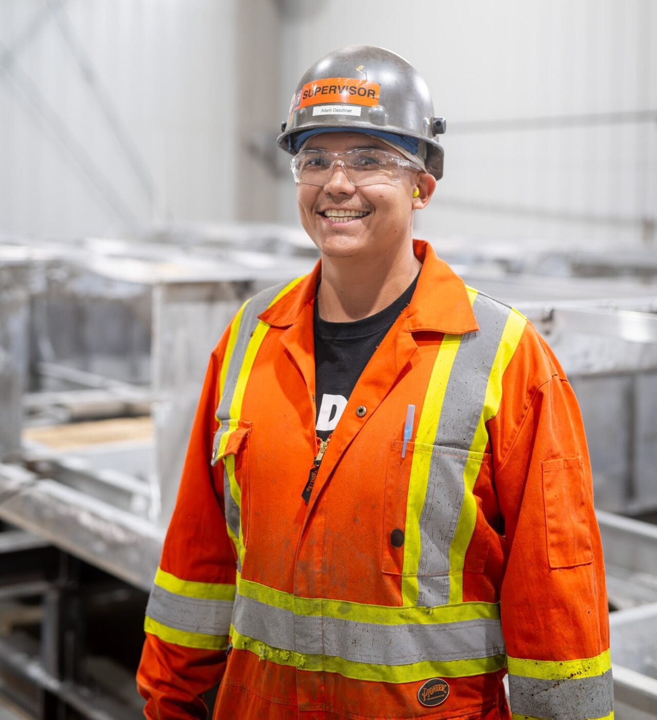 An Indigenous man wearing high-visibility coveralls and a hard hat.