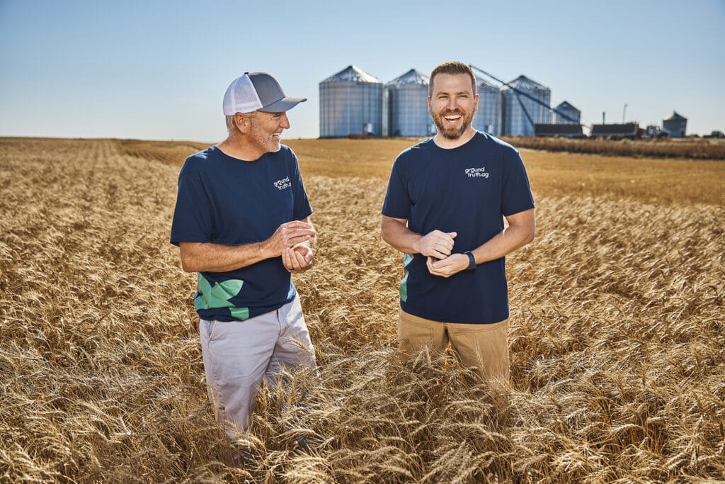 Two men in a wheat field, smiling.