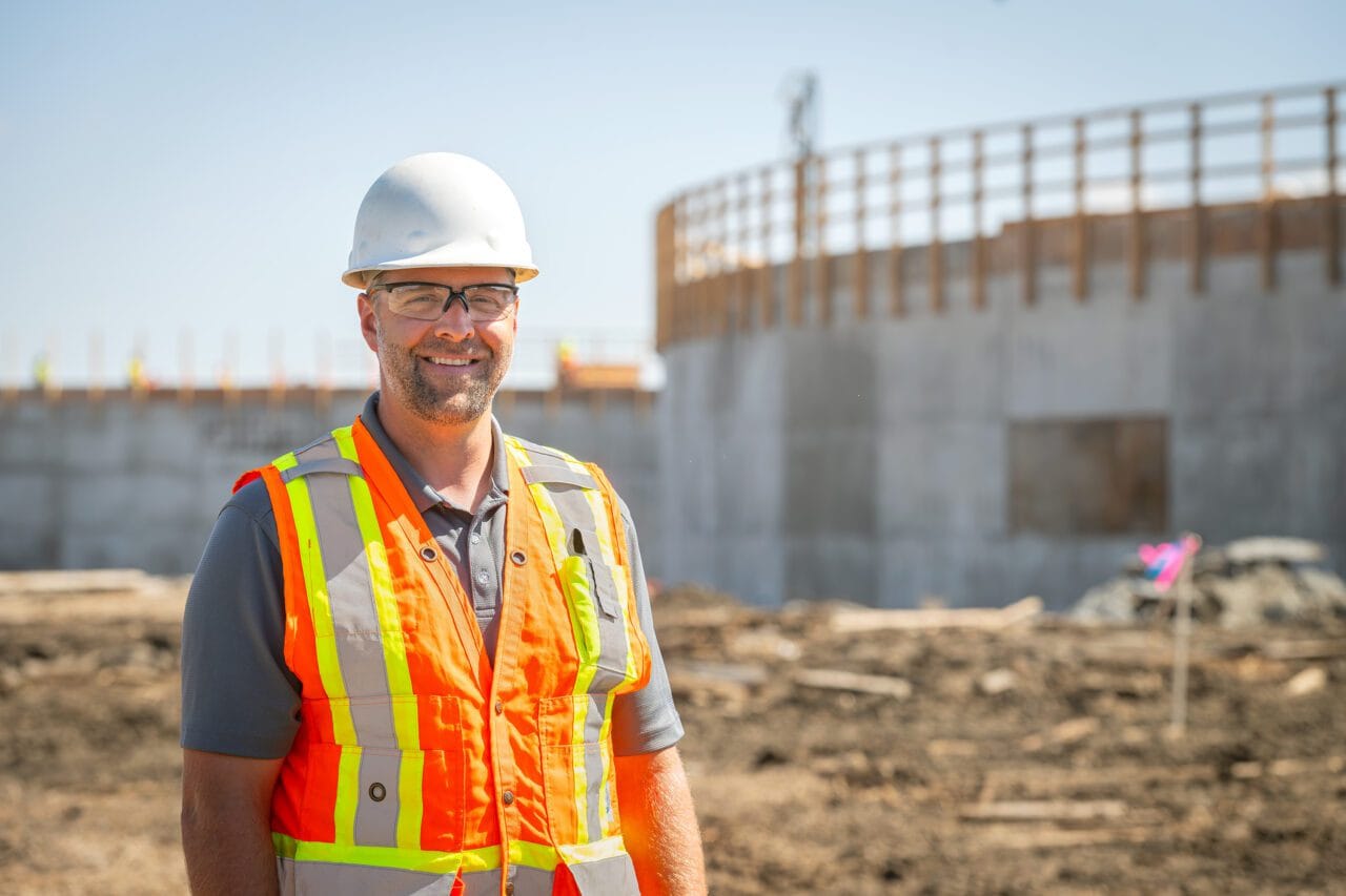 Colin Olfert wearing a white hard hat and safety vest while standing on a construction site.