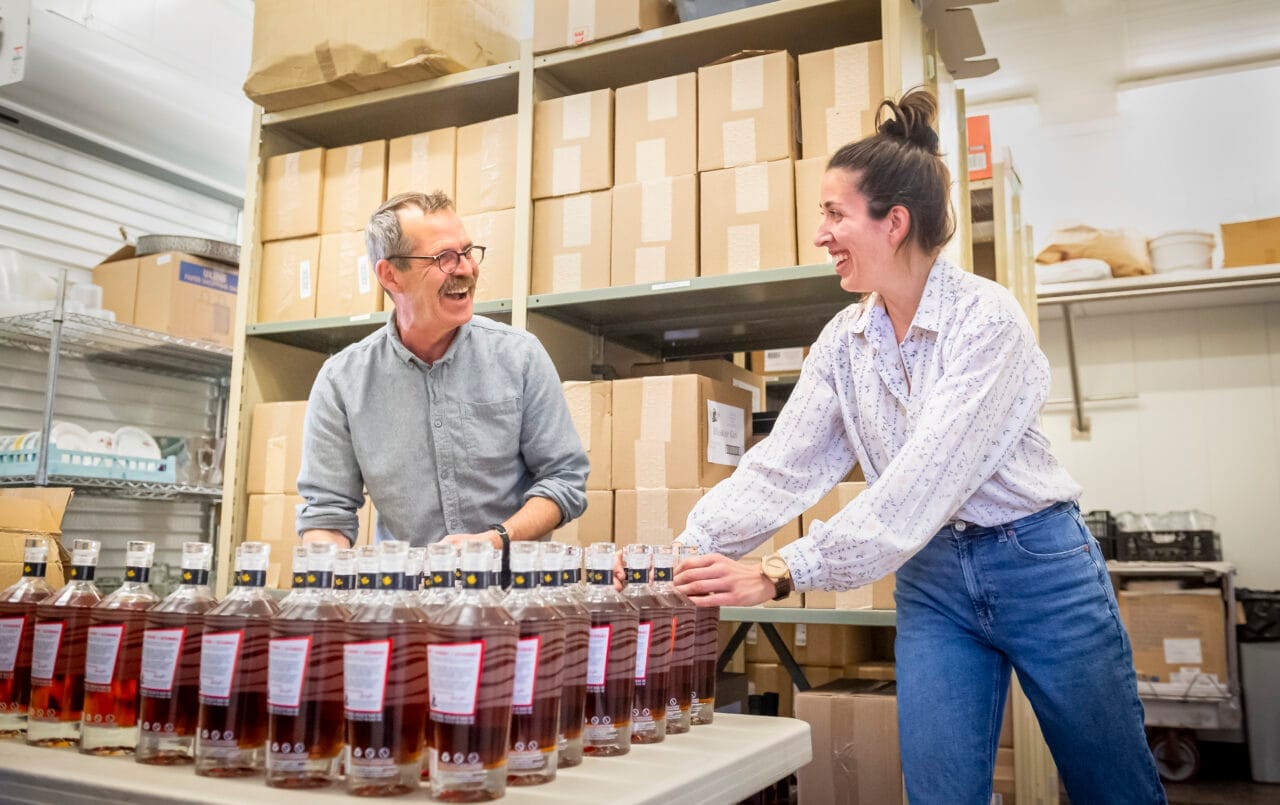 People packaging goods at a work table, placing products into containers as part of a small scale production or distribution process.