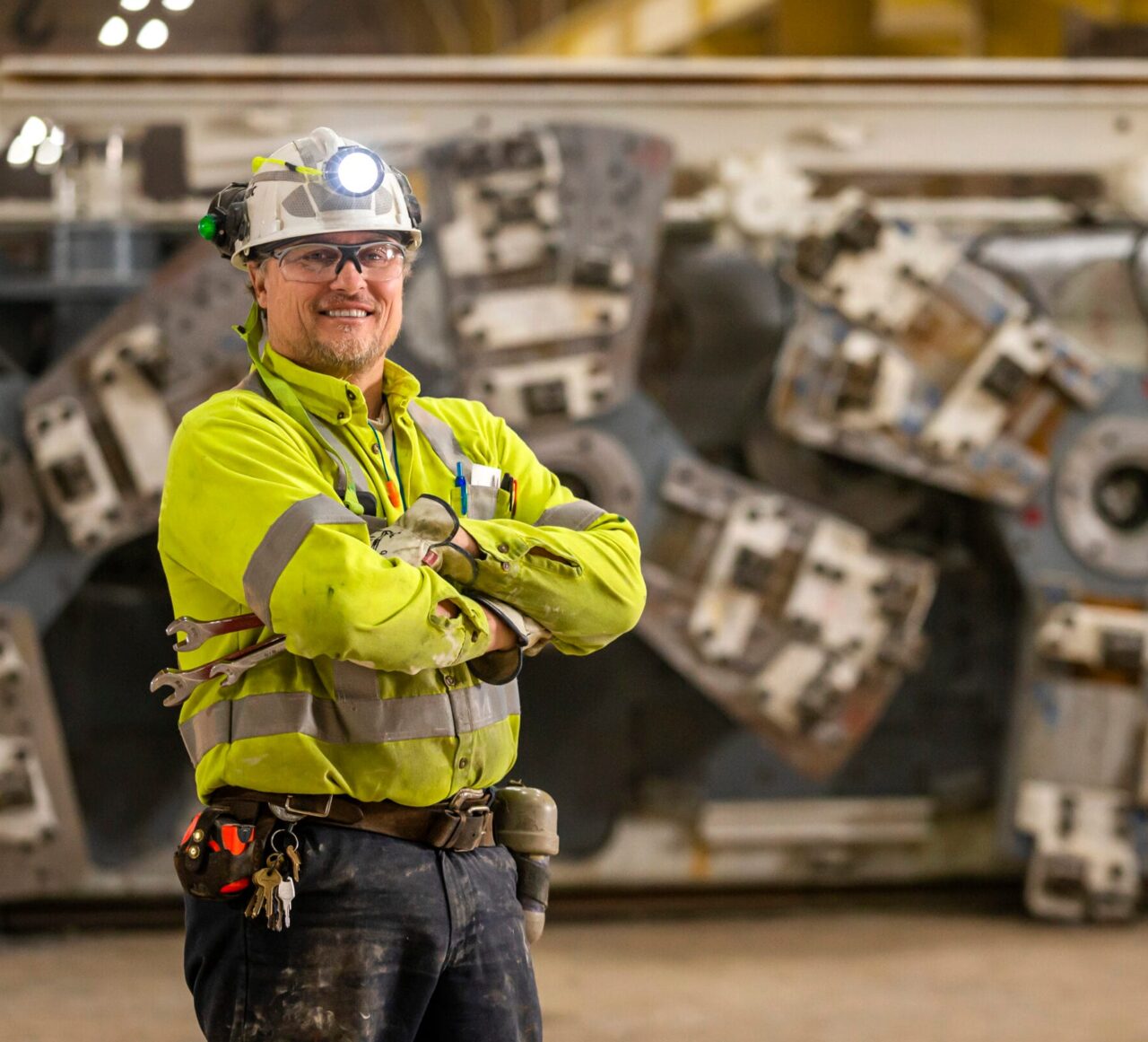 A man infront of heavy-duty mining equipment in full safety gear.