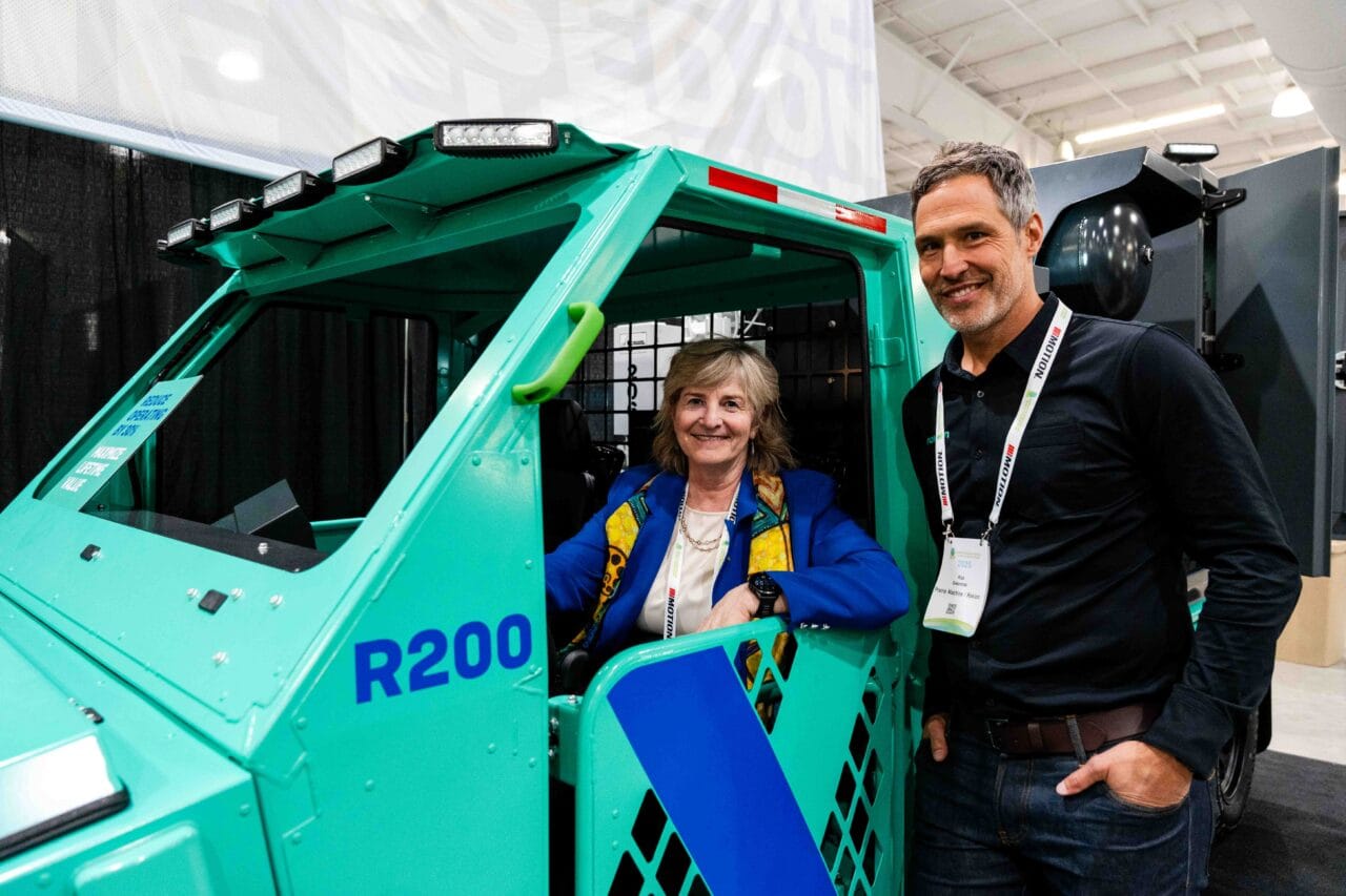 A woman sitting inside a vehicle used for mining and a man standing next to her.