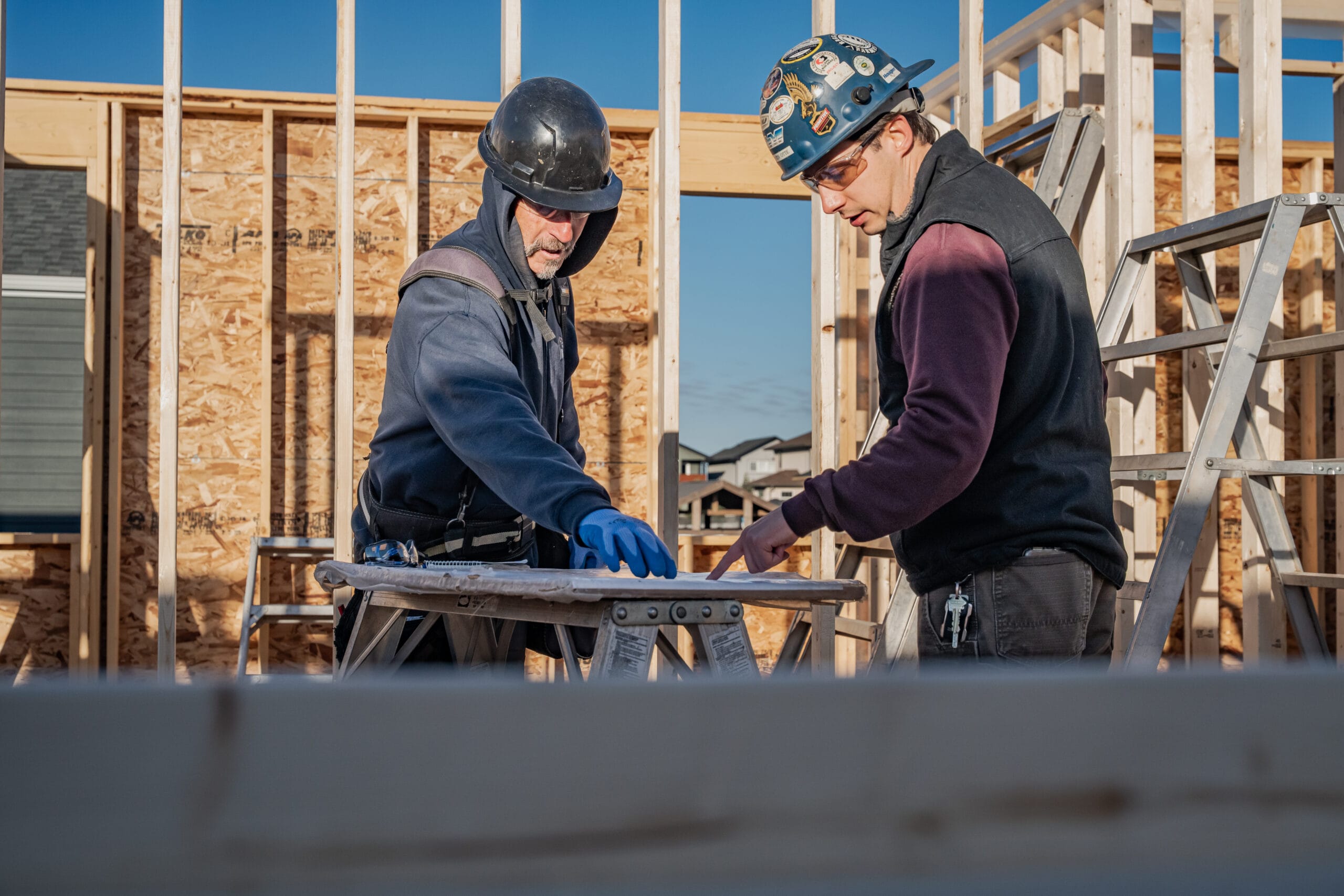 Two men in construction equipment review blueprints during a large home construction project.