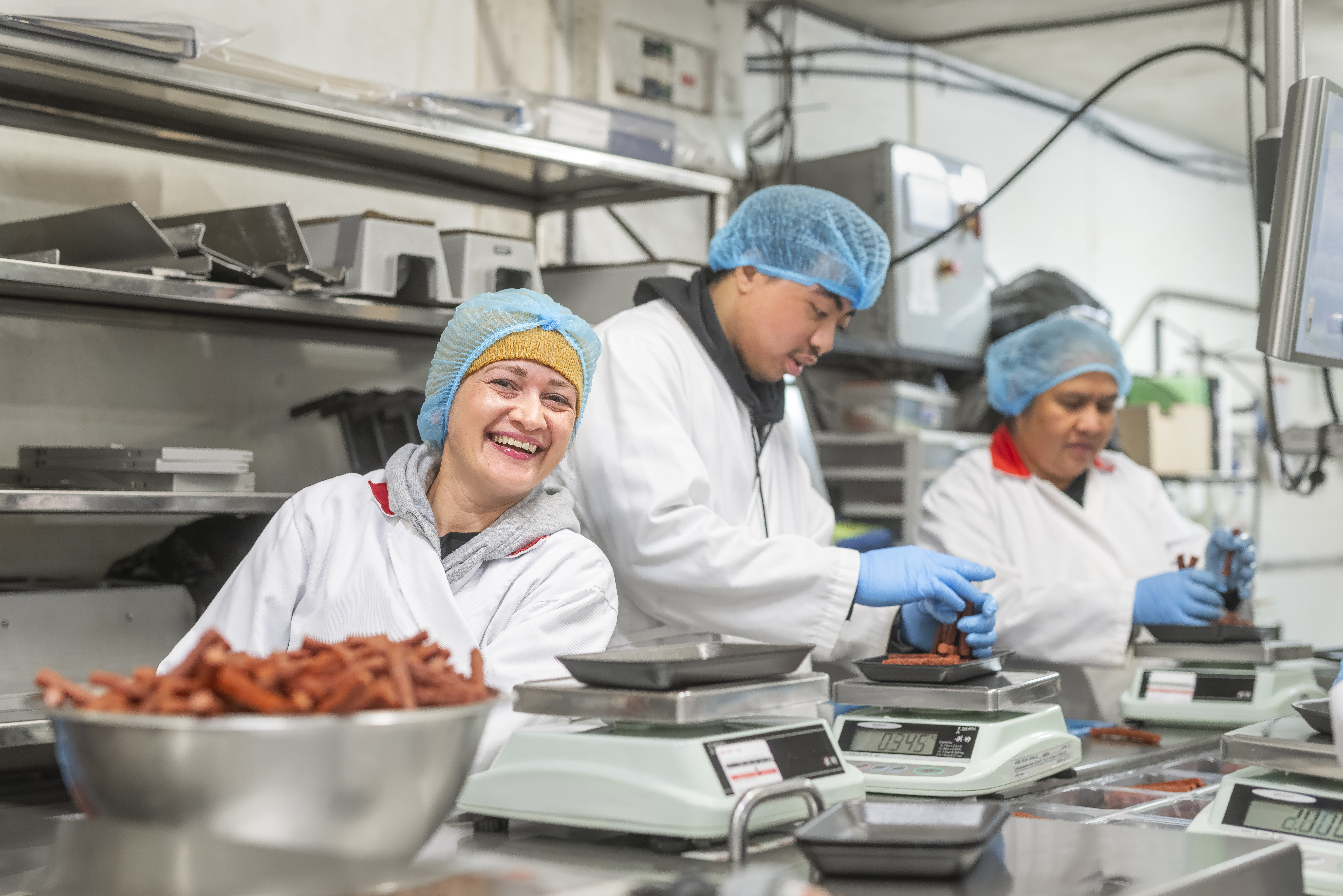 Image of three agriculture value added workers in a butcher shop actively working with meat processing equipment in a clean, professional facility.