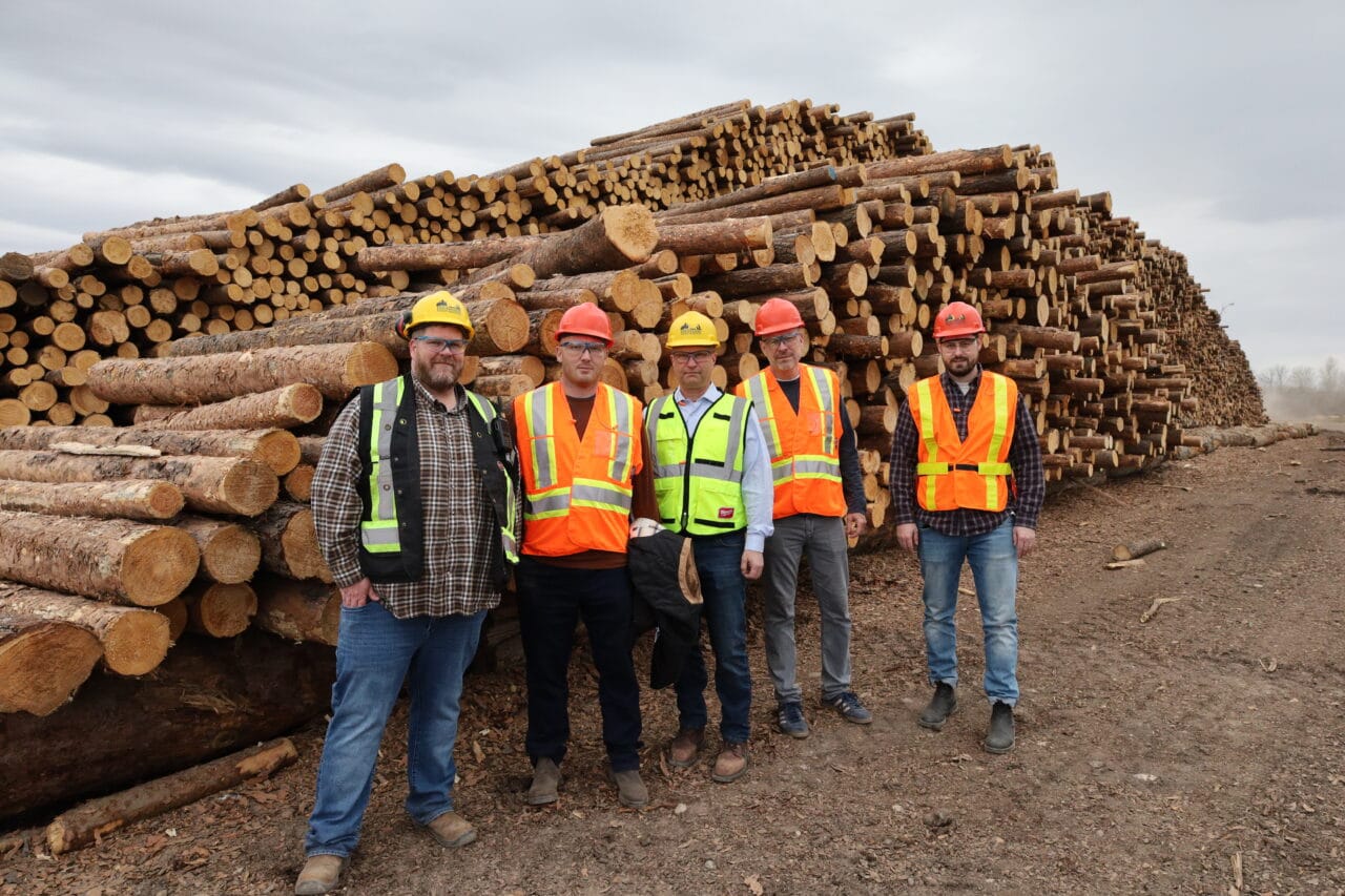 The Saskatchewan Minister for Energy and resources poses with Dunkley Lumber employees infront of a woodpile.