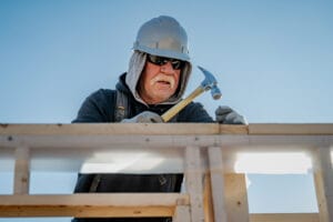 A man in construction gear hammers a nail.