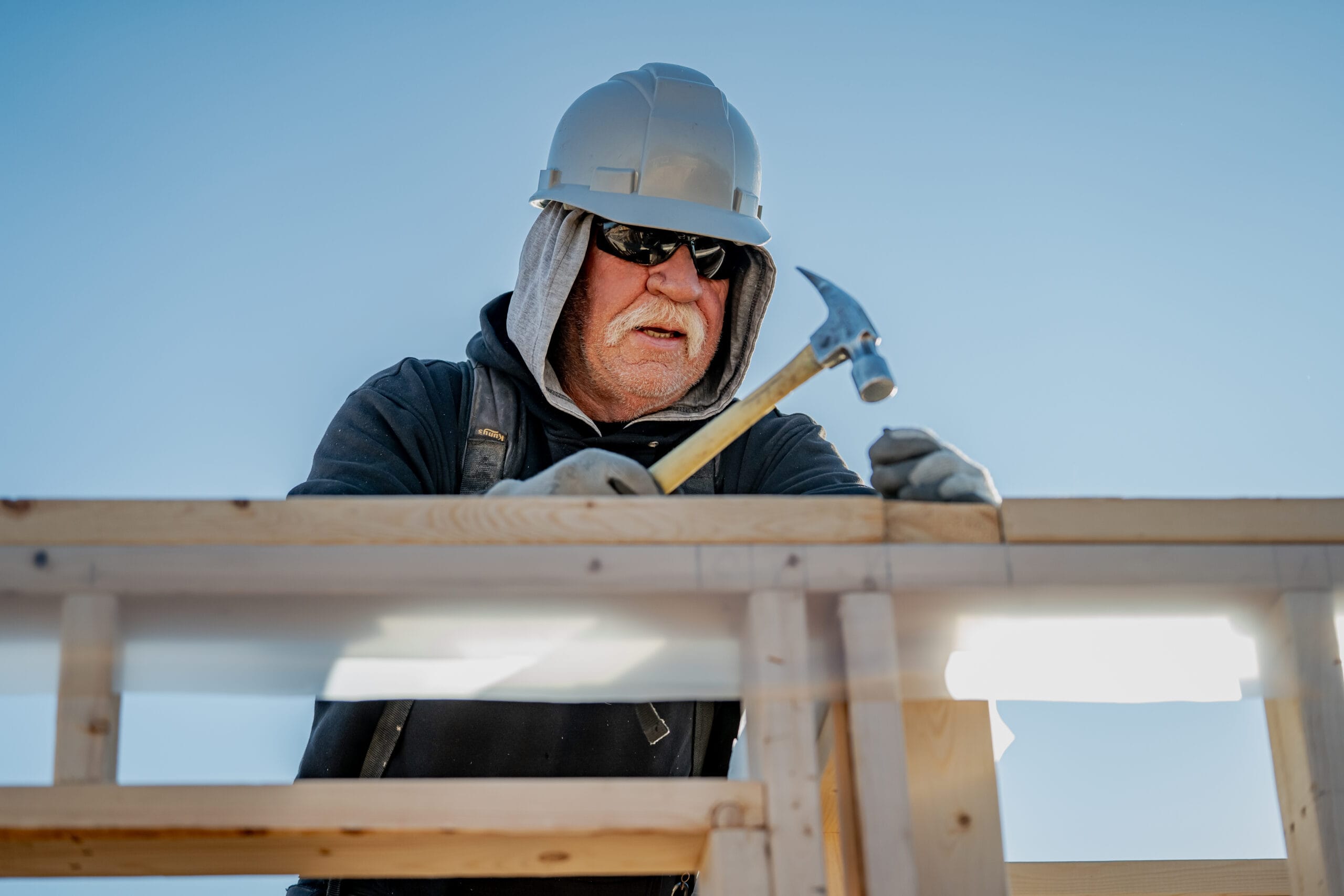 A man in construction gear hammers a nail.